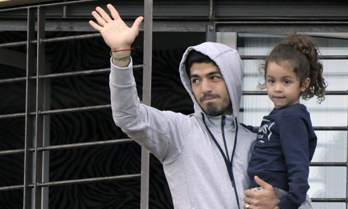 Uruguay's soccer player Luis Suarez holds his daughter as he greets fans from their home's balcony on the outskirts of Montevideo, Uruguay, Friday, June 27, 2014. Suarez returned to Montevideo early Friday, arriving too late to see the hundreds of Uruguay fans who had gathered the previous night to give him a hero's welcome despite his World Cup banishment. (AP Photo/Matilde Campodonico)