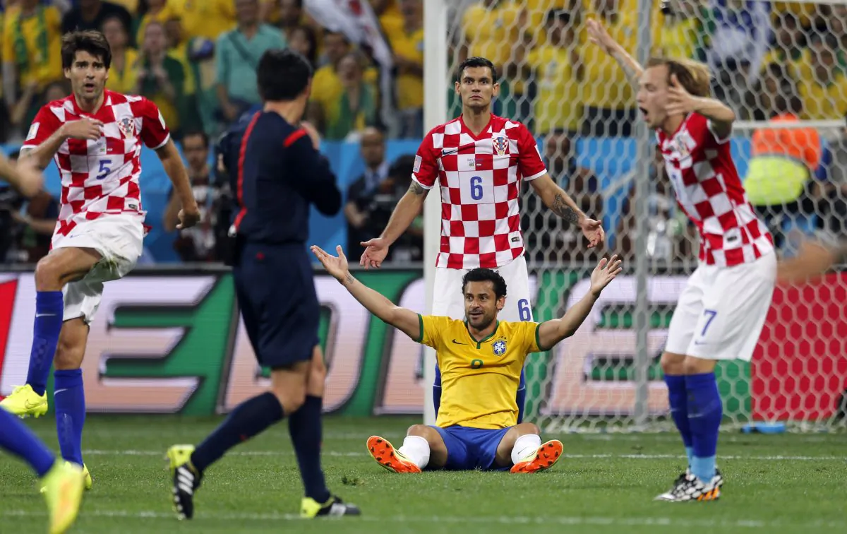 Brazil's Fred sits on the pitch as Croatian players Vedran Corluka (5), Dejan Lovren (6) and Ivan Rakitic (7) protest after referee Yuichi Nishimura, from Japan, called a penalty against Croatia during the group A World Cup soccer match in the opening game of the tournament at Itaquerao Stadium in Sao Paulo, Brazil, Thursday, June 12, 2014. Brazil's Neymar scored on a penalty kick after the play. (AP Photo/Frank Augstein)