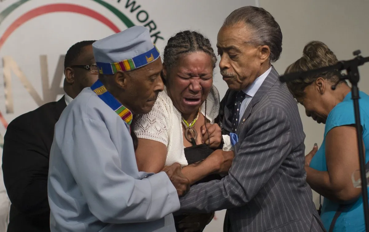 Esaw Garner, wife of Eric Garner, breaks down in the arms of Rev. Herbert Daughtry (L) and Rev. Al Sharpton during a rally at the National Action Network headquarters for Eric Garner on Saturday, July 19, 2014. (AP Photo/John Minchillo)