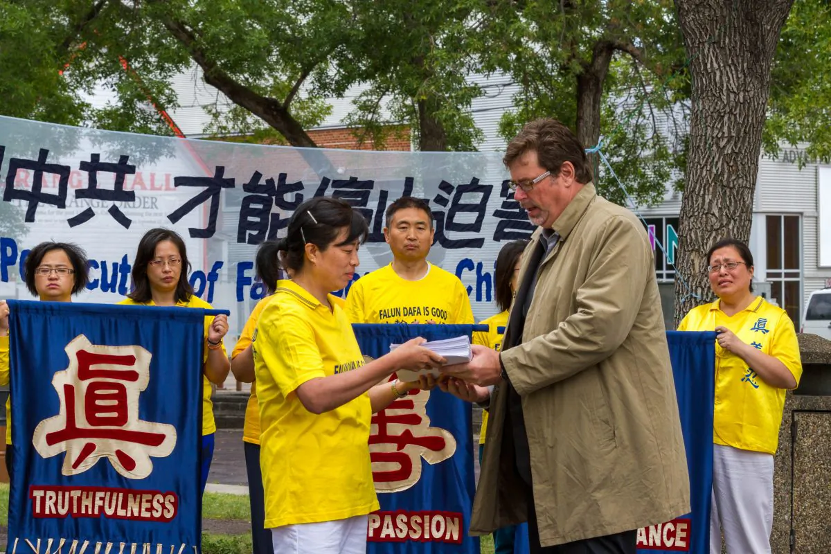 Dr. Minnan Liu (L) of the Falun Dafa Association of Edmonton presents over 4,000 signatures from Edmontonians on a petition to Brent Rathgeber, MP for Edmonton-St. Albert, on July 19, 2014 at the Dr. Wilbert McIntyre Park in Edmonton. The petition asks the Canadian government to urge the Chinese regime to stop the persecution of Falun Dafa in China. (Frank Liang/Epoch Times)