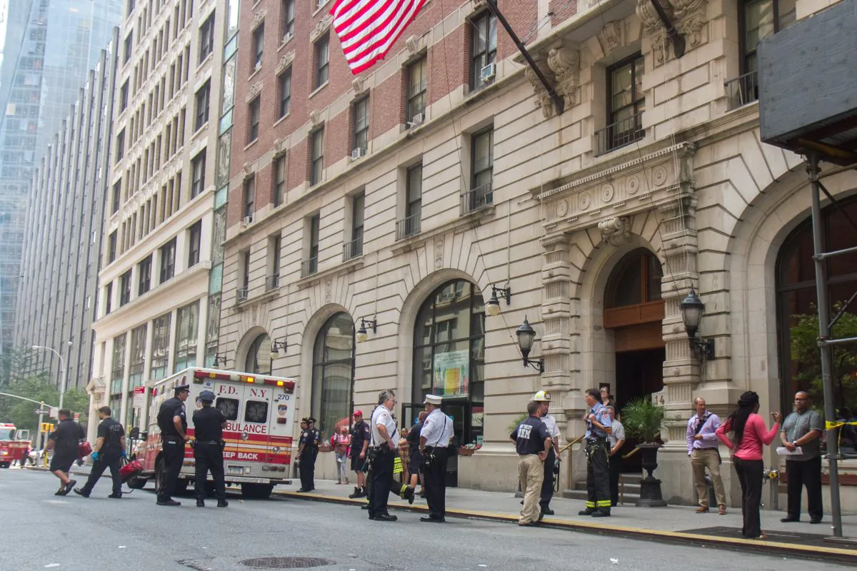 Fireman, policeman, and staff from the building where a fire broke out stand outside the building making sure the scene is secure, on 28th Street in Midtown Manhattan, New York, on July 29, 2014. (Benjamin Chasteen/Epoch Times)
