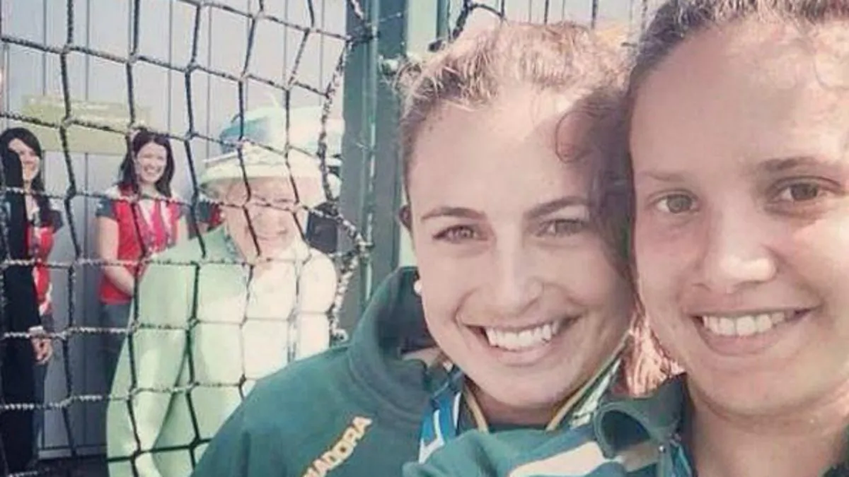 Hockeyroos Jade Taylor and Brooke Peris hit the jackpot when they took a ‘selfie’ at the Commonwealth Games in Glasgow on Thursday July 24, 2014. Hoping to catch the Queen in the background of a ‘selfie’ photo as she emerged from a doorway, Queen Elizabeth II immediately aware of what was happening made a broad smile at the smart phone. (Jade Taylor and Brooke Peris) 