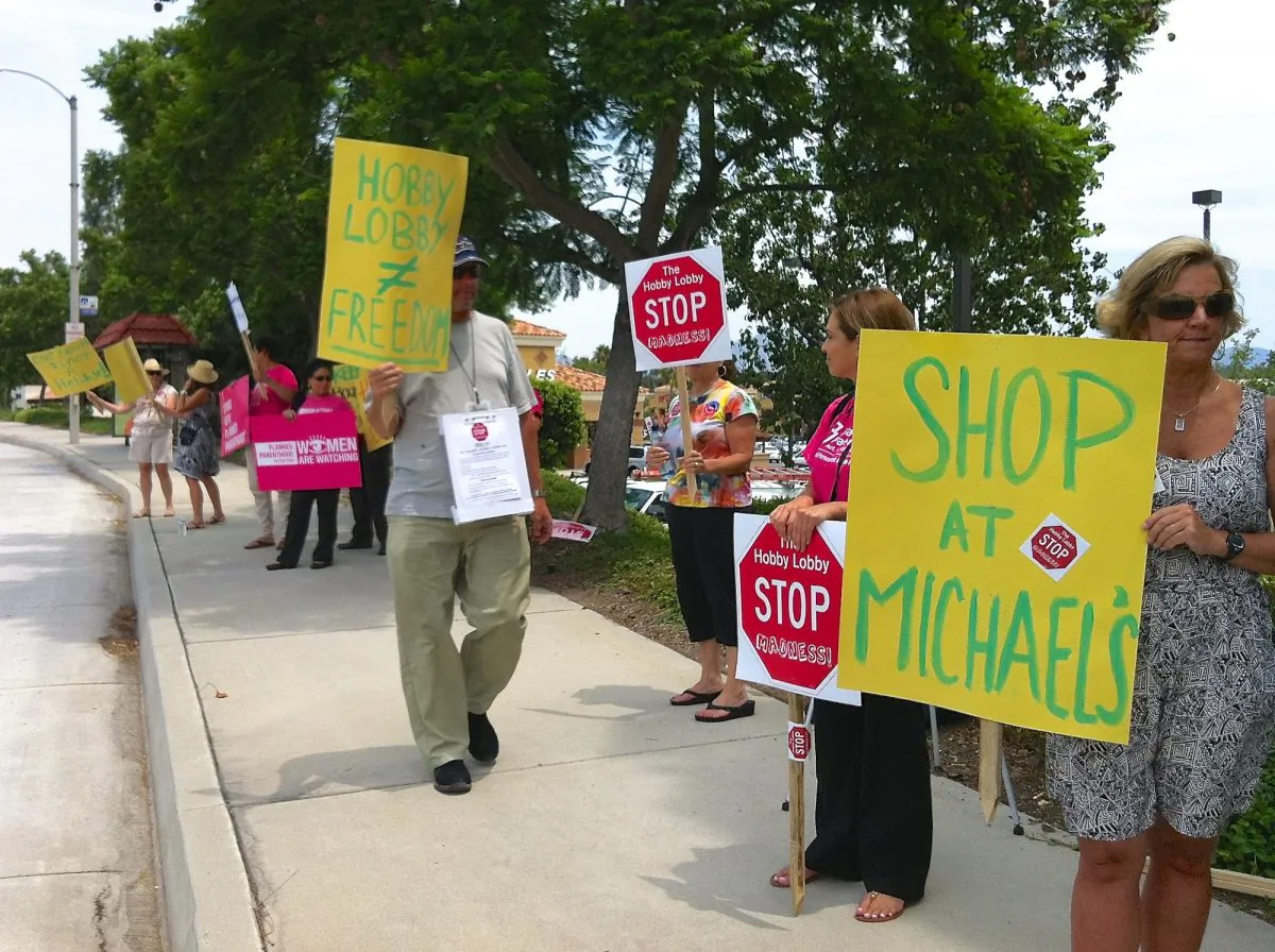 A group of protesters stands along the street outside of a business complex with a Hobby Lobby in Laguna Niguel, Calif., on July 29. (Sarah Le/Epoch Times)