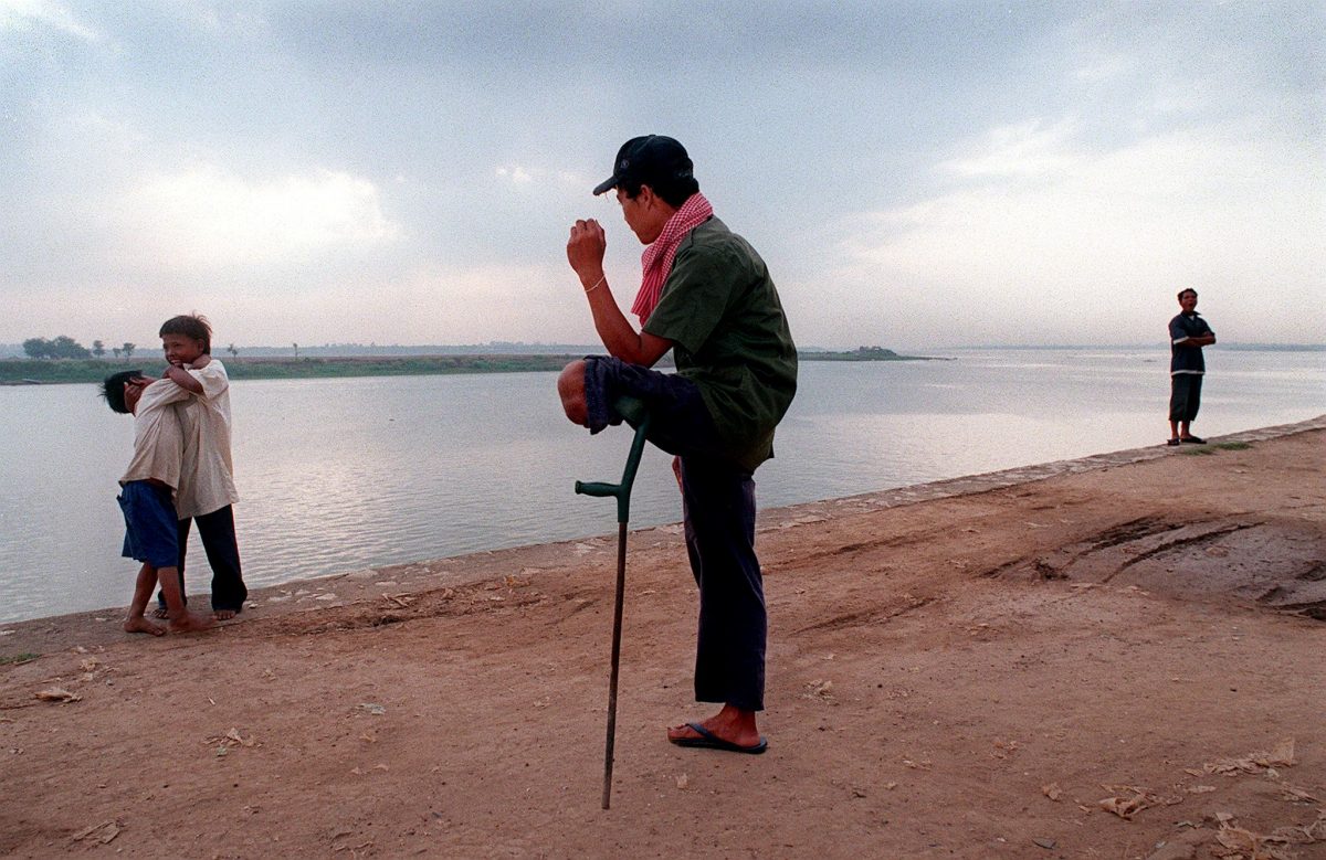 A Cambodian mine victim waiting for a hand-out from the next passing tourist rests on a crutch as he watches children scrap on the banks of the Tonle Sap River, Phnom Penh, April 9, 1999. (Rob Elliott/AFP/Getty Images)