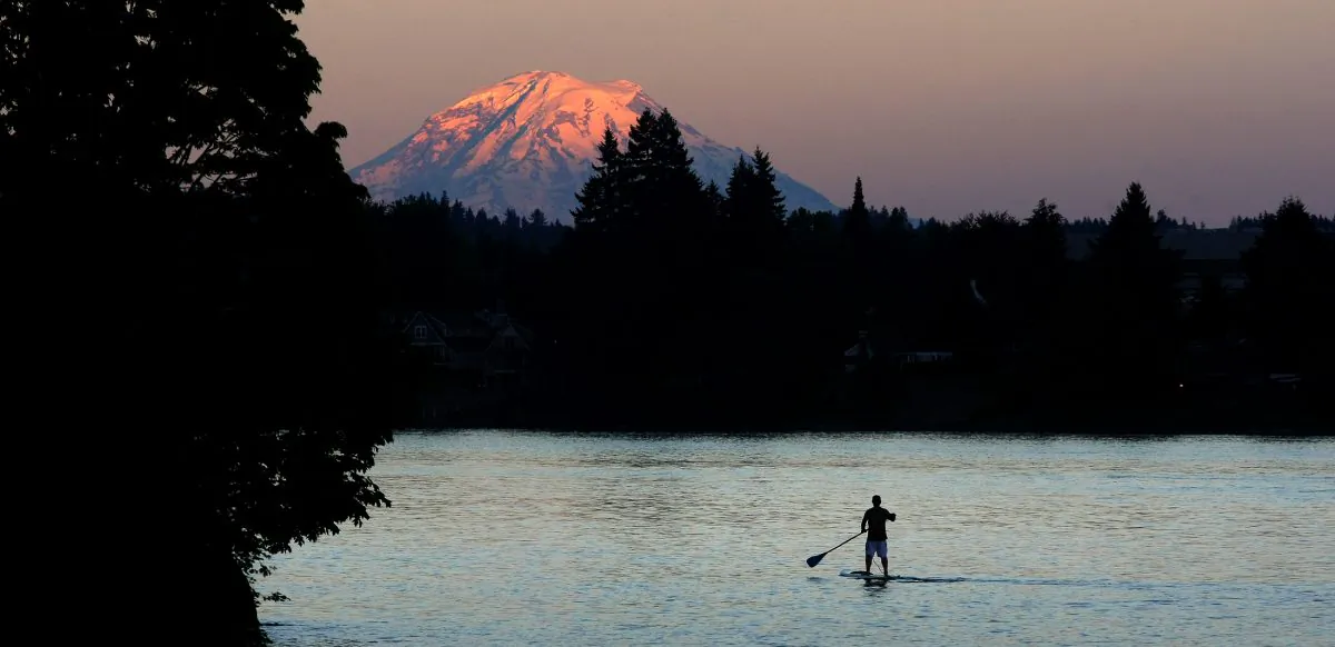 The top of Mount Rainier glows with the shades of the sunset as a paddle border goes past Pat Carey Park off Tracyton Blvd on July 1, 2014. (Kitsap Sun, Larry Steagall/AP Photo)