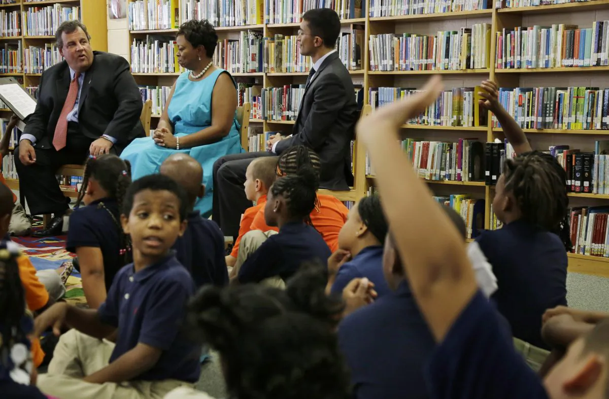 Elementary school students raise their hands to ask New Jersey Gov. Chris Christie (seated, L) a question, as Camden Mayor Dana Redd (seated, C) and Camden schools superintendent Paymon Rouhanifard (seated, R) look on, during a meeting at Riletta Twyne Cream school in Camden, N.J. on Sept. 10, 2013. New Jersey's state government has been giving a lot of attention to its poorest city, but some activists in Camden don't think the help is going to the right places. (Mel Evans/AP)