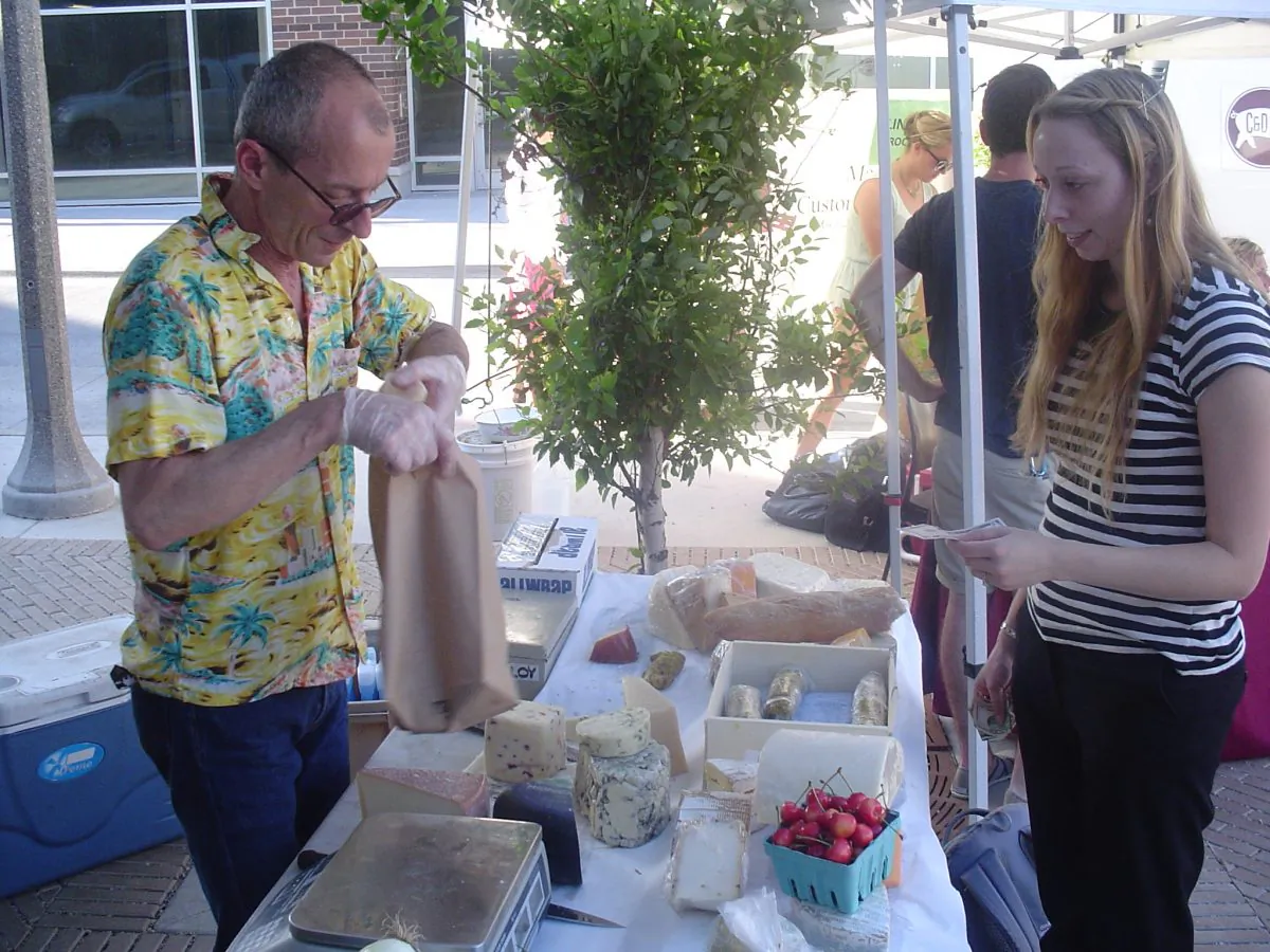 At a Chicago farmer’s market, cheese seller Mike Stumm wraps a selection for high school math teacher, Kat Bennett. (Conan Milner/Epoch Times)