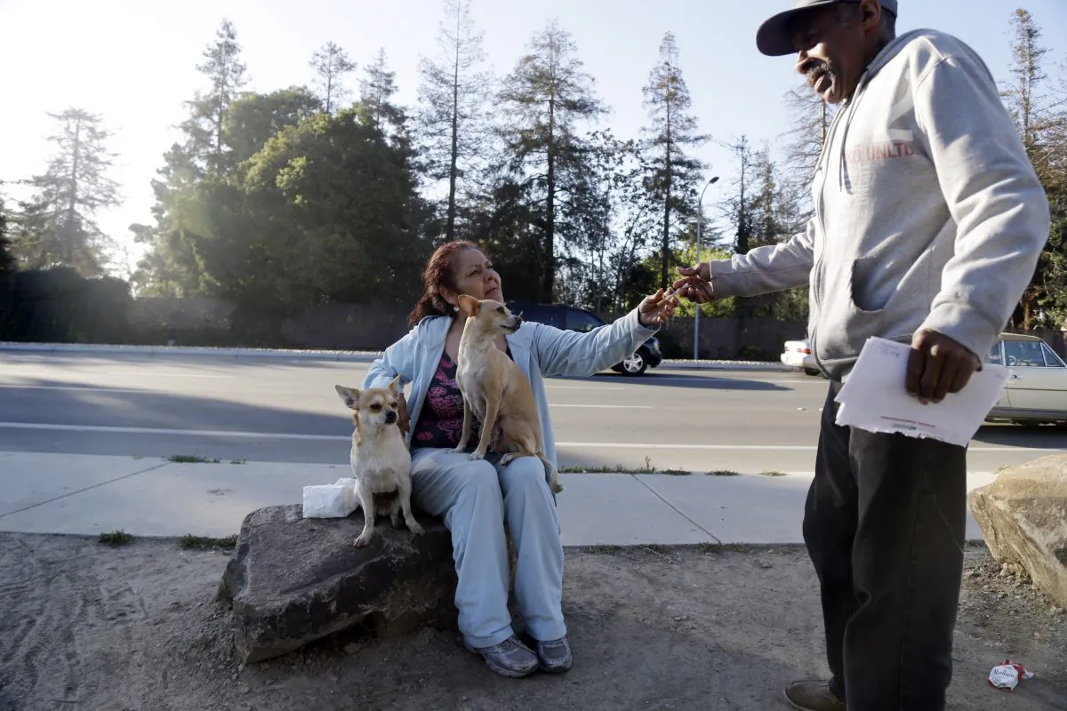 In this March 18, 2014, photo Maria Esther Salazar (C) grabs a cigarette from a friend in the Jungle, a homeless encampment in San Jose, Calif. The Jungle and several hundred smaller encampments in the region are the consequence of urban sprawl, with large open spaces that are not parks, and thus without rangers. (AP Photo/Marcio Jose Sanchez)