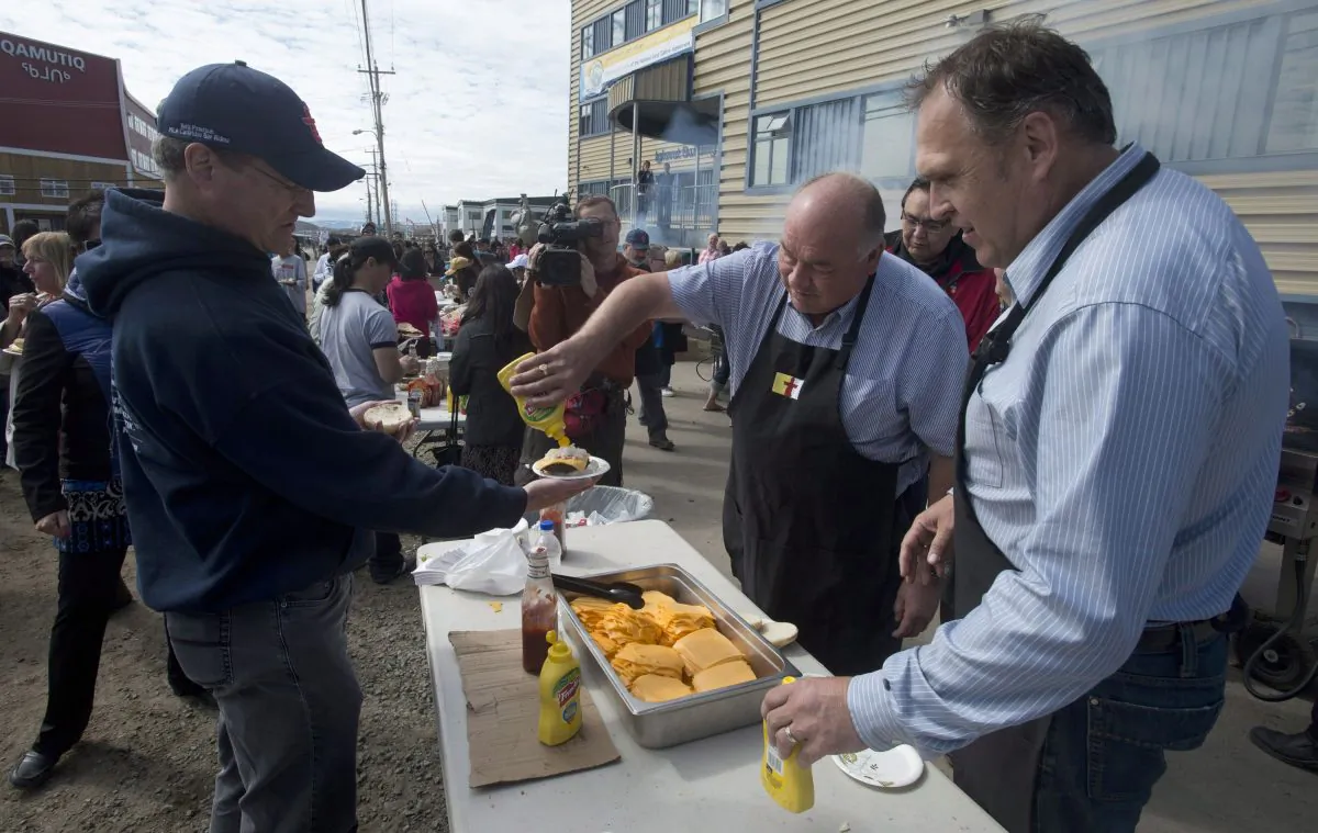 Yukon Premier Darrell Pasloski (R) and Northwest Territories Premier Bob McLeod serve a man a hamburger during Nunavut Day celebrations on July 9, 2014, in Iqaluit. The premiers of six western provinces and territories are in Nunavut for a gathering expected to focus on natural resources development and its impact on northern and remote communities. (The Canadian Press/Adrian Wyld)