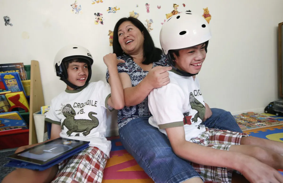 Arlene Aguirre (C) plays with her formerly conjoined twin sons, Clarence (L) and Carl, 12, at the family's home in Scarsdale, N.Y., Thursday, July 31, 2014. On Monday, Aug. 4, the family will celebrate the 10th anniversary of the risky surgery in which the boys were separated at Montefiore Hospital, where the surgery was initially performed. (AP Photo/Kathy Willens)