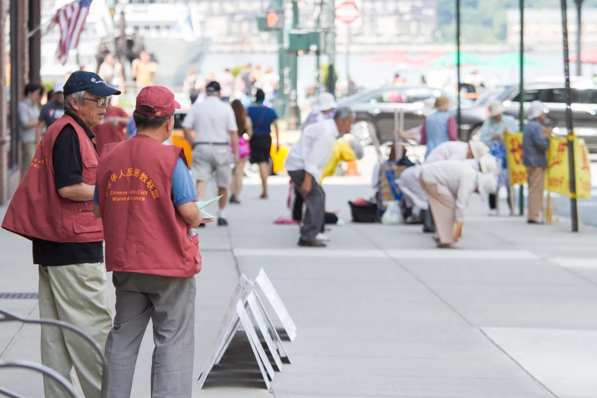 Two Chinese people hand out CCPs hate materials against the peaceful spiritual practice of Falun Gong next to practitioners performing the exercise of the practice, in front of the Chinese Consulate, in Manhattan, on Aug. 5, 2014. (Benjamin Chasteen/Epoch Times)