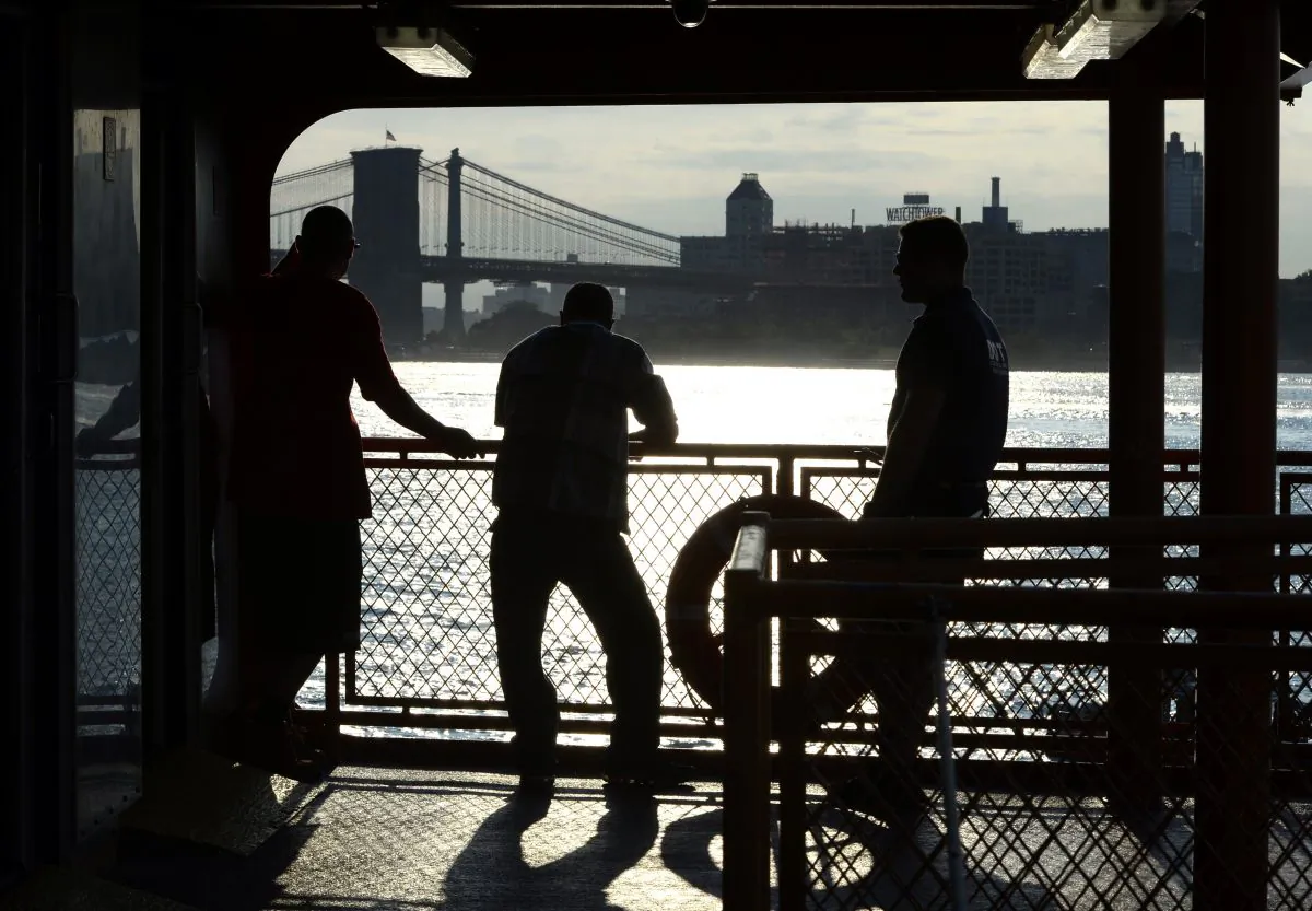 With the Brooklyn Bridge in the background, commuters on the Staten Island Ferry watch the morning sunrise in the New York Harbor in lower Manhattan, on July 11, 2014. (Timothy A. Clary/AFP/Getty Images)
