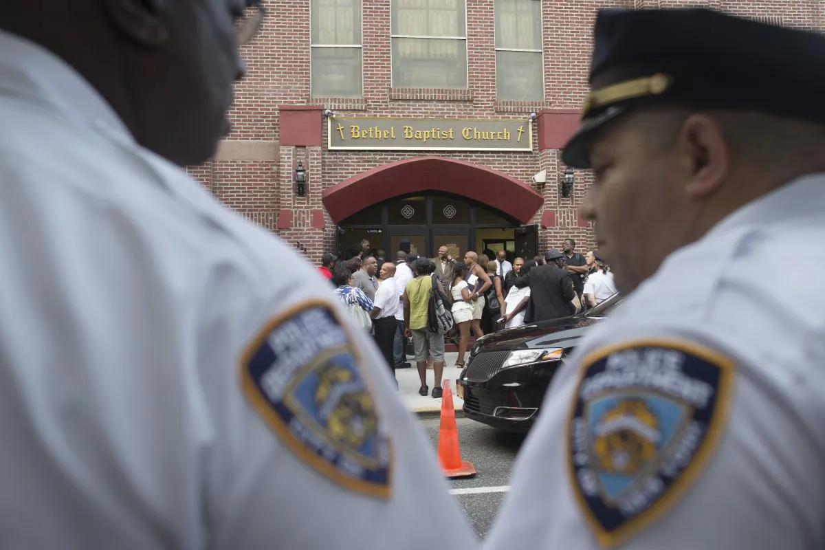 In this July 23, 2014, photo, a pair of New York City police officers stand at their post as mourners arrive for the funeral service of Eric Garner at Bethel Baptist Church in the Brooklyn borough of New York. Garner died on July 17, 2014. (AP Photo/John Minchillo)