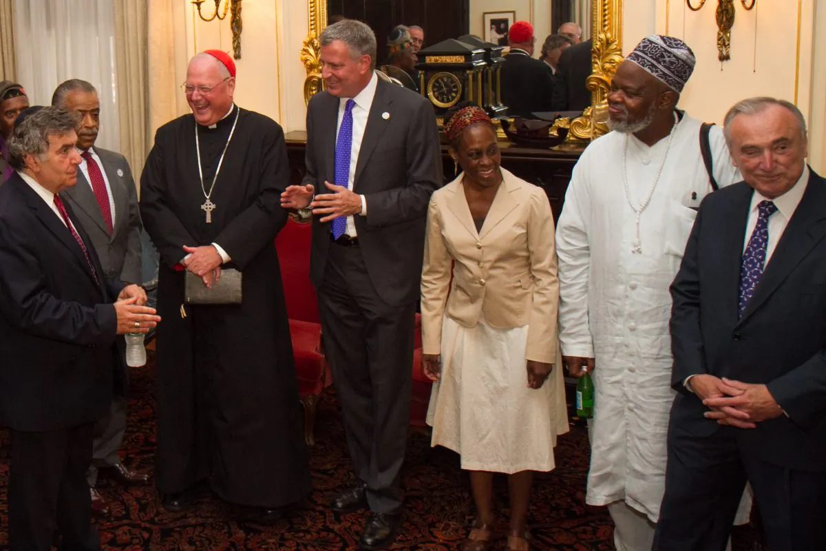 NYC Mayor Bill de Blasio (C) along with his wife (3rd R) meets with Timothy Cardinal Dolan, (3rd L) Rev. Al Sharpton, (2nd L) and commissioner William Bratton, (R) and other clergy members, for an interfaith roundtable meeting in Manhattan, New York on Wednesday, Aug. 20, 2014. (Benjamin Chasteen/Epoch Times)