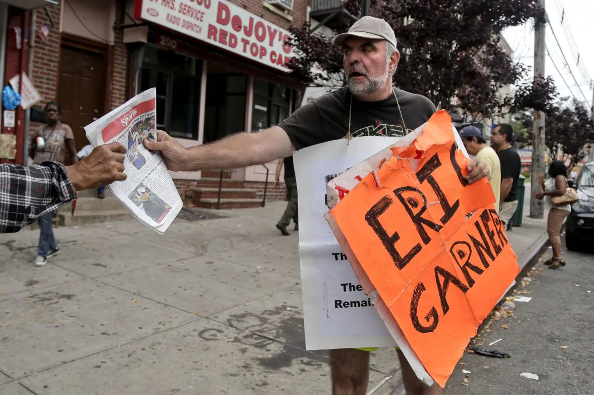 Doug Phaneuf hands a newspaper to a pedestrian while offering information to passers-by about a rally for Eric Garner, Friday, Aug. 1, 2014, in the Staten Island borough of New York. Garner died after he was put in a chokehold while being arrested last month for selling untaxed loose cigarettes. On Friday, the medical examiner ruled Garner's death to be a homicide caused by a police chokehold. (AP Photo/Julie Jacobson)