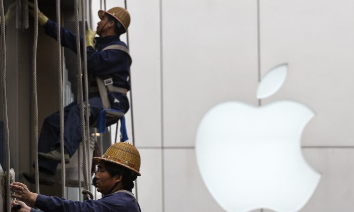 In this April 10, 2014 photo, workers clean windows near Apple's retail store in Beijing, China. An Apple supplier in China is violating safety and pay rules despite the computer giant’s promises to improve conditions, two activist groups said Thursday, Sept. 4, 2014, ahead of the release of the iPhone 6. (AP Photo/Andy Wong)