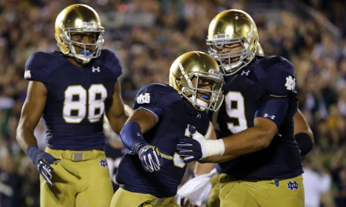 Notre Dame wide receiver Amir Carlisle, center, celebrates a touchdown with offensive linesman Steve Elmer, right, and wide receiver Buster Sheridan during the second half of an NCAA college football game against Michigan in South Bend, Ind., Saturday, Sept. 6, 2014. (AP Photo/Michael Conroy)