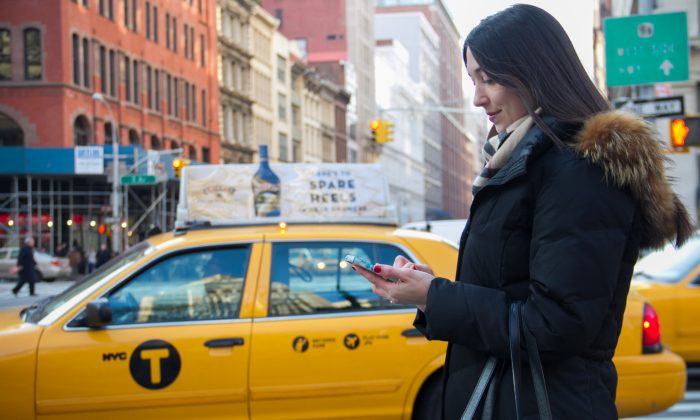 Vanessa Panotas, uses her iPhone on 23rd Street in New York City while a NYC taxi drives by on Nov. 29, 2012. Already in use in Chigaco and Boston, New Yorkers may soon be able to hail taxis using their smartphones. (Benjamin Chasteen/The Epoch Times)