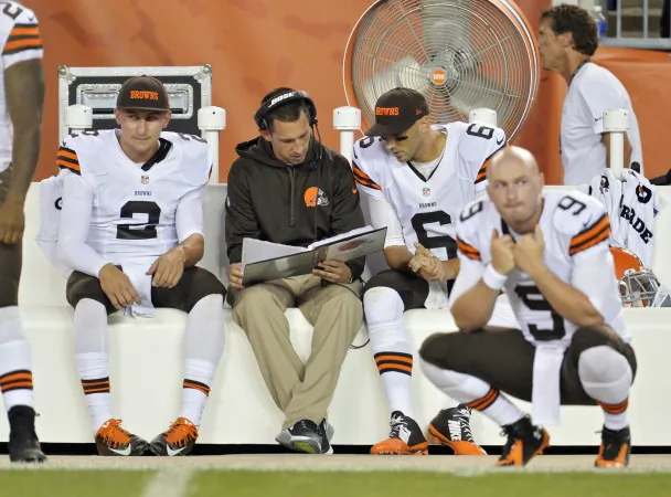 FILE - In this Aug. 23, 2014, file photo, Cleveland Browns quarterbacks Johnny Manziel (2) listens in as offensive coordinator Kyle Shanahan, center, talks with Brian Hoyer (6) on the sidelines in the fourth quarter of a preseason NFL football game against the St. Louis Rams in Cleveland. Manziel doesn't view himself as the Browns' savior, but almost everyone else does. The dynamic rookie quarterback will begin the season as Cleveland's second-string quarterback, but it may not be long before he's moved ahead of Hoyer, who already seems to be looking over his shoulder. (AP Photo/David Richard, File)