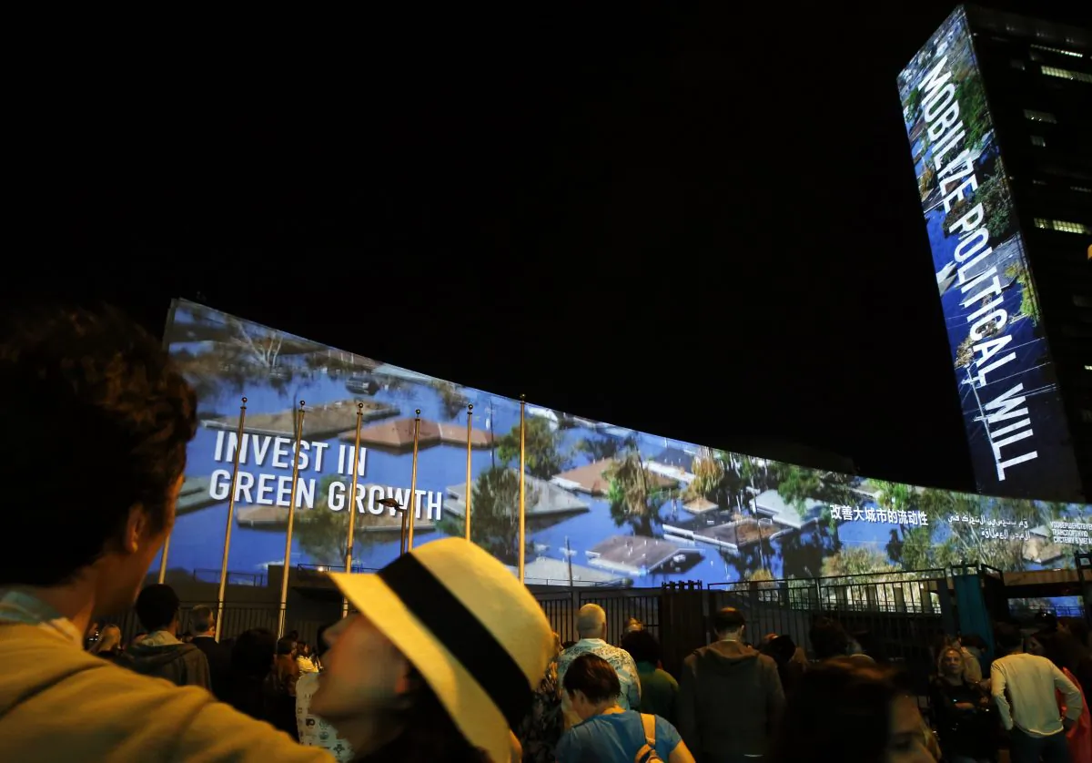 A crowd gathers outside as an architectural light show entitled illUmiNations: Protecting Our Planet, designed to inspire action on climate change, is projected on the side of United Nations headquarters Saturday, Sept. 20, 2014.  (AP Photo/Jason DeCrow)