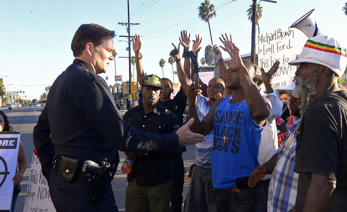 In this photo, protesters hold their hands up as a Los Angeles Police Department officer tries to talk to them in front of the 77th Street police station in Los Angeles during a protest of the LAPD shooting of Ezell Ford on Aug. 14, 2014. Police say that Ford had attempted to remove a gun from an officer's holster on Aug. 11 when he was shot and killed, which differs from accounts by the family of the man. (Mark J. Terrill/AP Photo)