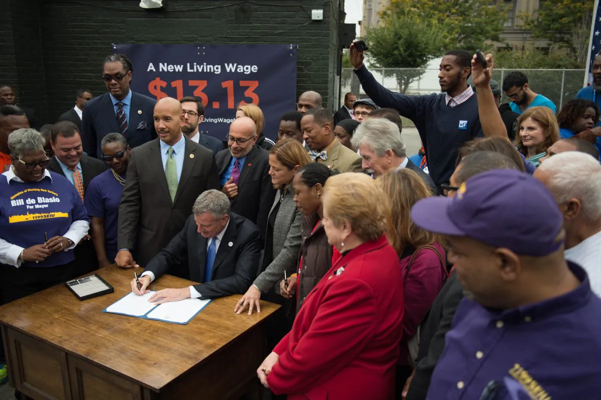 New York City Mayor Bill de Blasio signs an executive order to raise the living wage for workers employed at city-subsidized developments, at St. Mary's Park in the Bronx, N.Y., on Sept. 30, 2014. Workers will now earn $13.13 an hour, and retail tenants at the developments will also be required to pay the higher rate. (The New York City Mayor's Office)