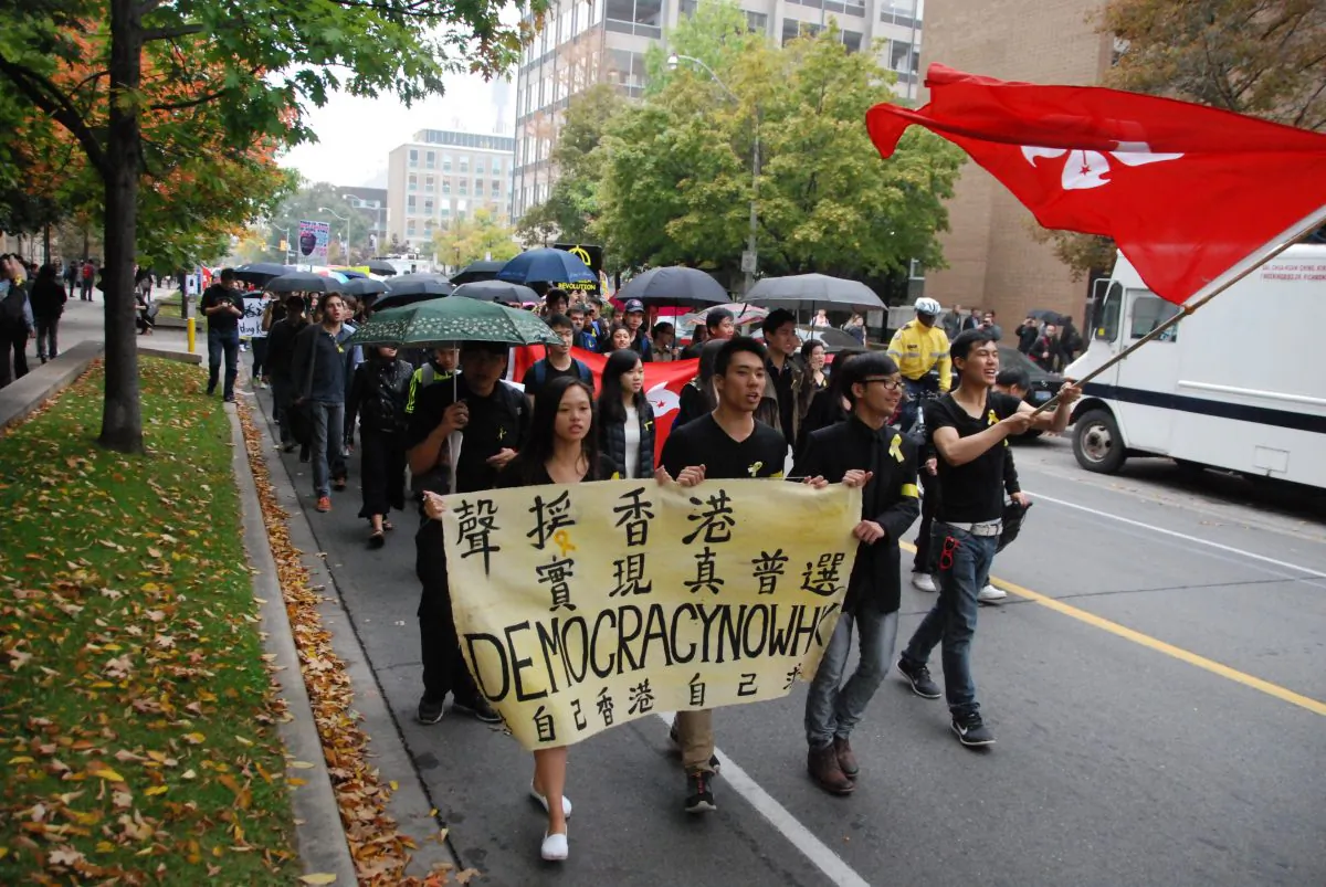People carry umbrellas on a street in Toronto on Oct. 1, 2014 while demonstrating in solidarity with protesters in Hong Kong. Supporters of democracy took to Hong Kong's streets after the Chinese regime ruled that it would restrict who could run in the 2017 election for the island city's chief executive. (Ling Yi/Epoch Times)
