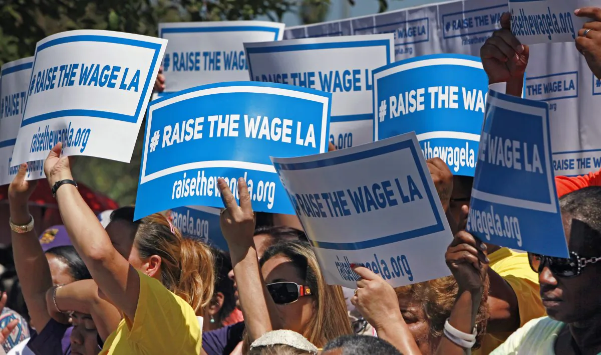 Supporters carry signs to raise the minimum wage in Los Angeles as they listen to Mayor Eric Garcetti during an announcement at the Martin Luther King Jr. Park with a coalition of business, labor, community, and faith leaders from across the city on Sept. 1, 2014. Garcetti announced his proposal to raise the minimum wage in Los Angeles from the current $9 an hour to $15 in 2020. (Richard Vogel/AP)