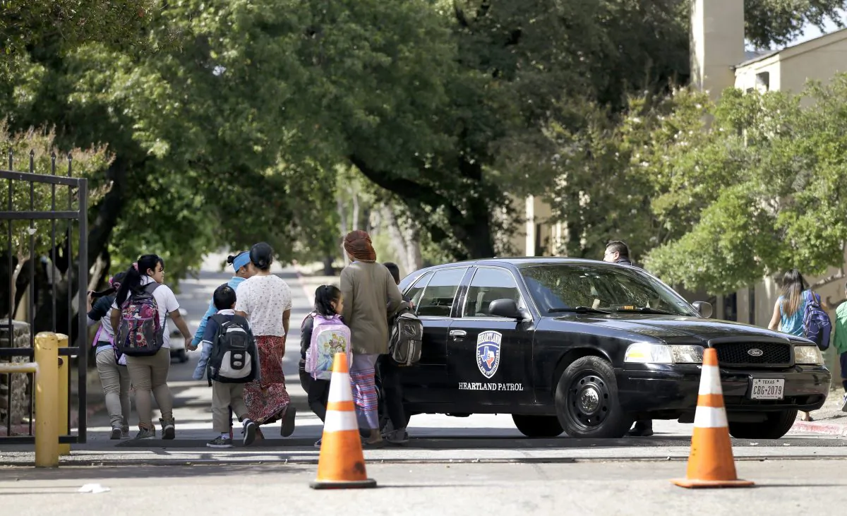 Families walk by a law enforcement vehicle near the main entrance to The Ivy Apartments as children return from school, Wednesday, Oct. 1, 2014, in Dallas. The man diagnosed with having the Ebola virus was staying at the complex with family and is now hospitalized. (AP Photo/Tony Gutierrez)