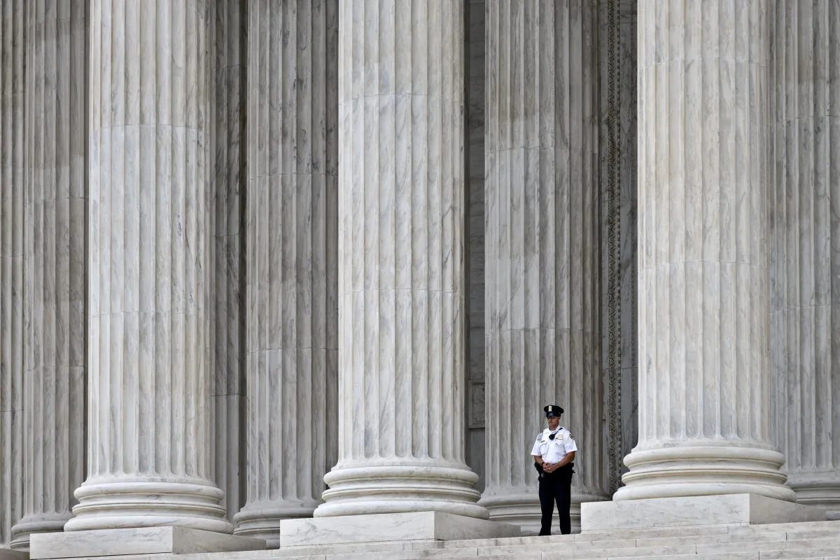 In this Oct. 7, 2014, photo, a police officer is dwarfed amid the marble columns of the Supreme Court in Washington. Some warehouse workers who fill orders for Amazon.com customers say they spend up to 25 minutes after every shift waiting to pass through security checks to make sure they aren't stealing from the online retailer. But they don't get paid for the extra time. The Supreme Court hears arguments Wednesday in a lawsuit filed by two former staffers at a Nevada warehouse who claim they should be compensated for time spent in security screenings under the Fair Labor Standards Act.  (AP Photo/J. Scott Applewhite)
