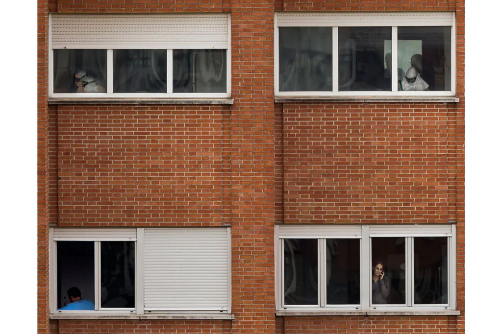 Medical practitioners wearing protective clothing work while Javier Limon, the husband of the nursing assistant infected with Ebola, is seen through a window, down left, while another isolated girl talks on her phone inside an isolated ward on the sixth floor of the the Carlos III hospital in Madrid, Spain, Friday, Oct. 10, 2014. A Spanish hospital official says the nursing assistant infected with Ebola is "stable," hours after authorities described her condition as critical. She is the first person known to have caught the disease outside the outbreak zone in West Africa. She contracted the virus while helping treat a Spanish missionary who became infected in West Africa, and later died. (AP Photo/Daniel Ochoa de Olza)