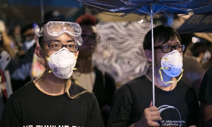Pro-democracy protesters stand behind barricades as police stand guard on the other side on Lung Wo Road, one of the major roadways in Hong Kong, on Oct. 14, 2014. (Benjamin Chasteen/Epoch Times)