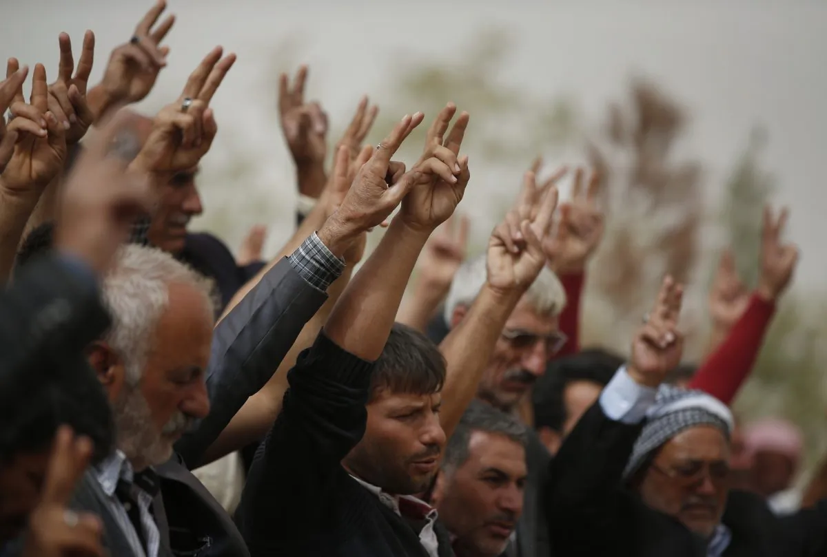 Mourners flash the victory sign on Oct. 11, 2014, as they sing a nationalistic Kurdish song at a cemetery in Suruc, Turkey during the funeral of two Syrian Kurdish fighters, who were killed in fighting with militants of the Islamic State group in Kobani, Syria. No one contests that the US-led coalition has conducted more than 40 airstrikes against the militants besieging Kobani, nor that Turkey has granted refuge to more than 200,000 people who have flooded across the border to escape the offensive. But Kurds say that both countries - and the international community in general - should be doing more to help save Kobani from the fanatical militants who have massacred and beheaded their enemies across Syria and Iraq. (AP Photo/Lefteris Pitarakis)