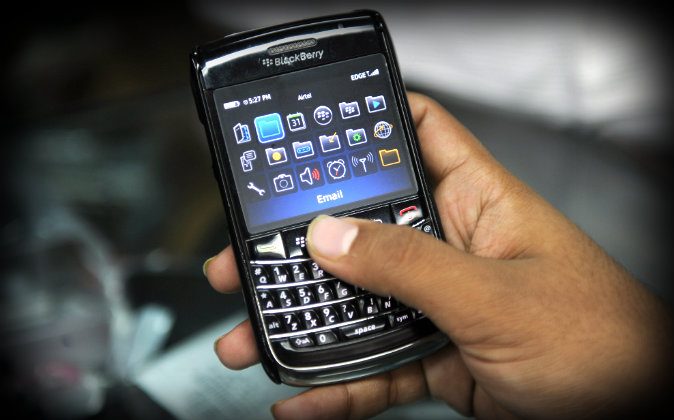 An Indian salesman checks a phone given for repairs at a Blackberry store in Mumbai on August 13, 2010. (Indranil Mukherjee/AFP/Getty Images; effects added by Epoch Times)