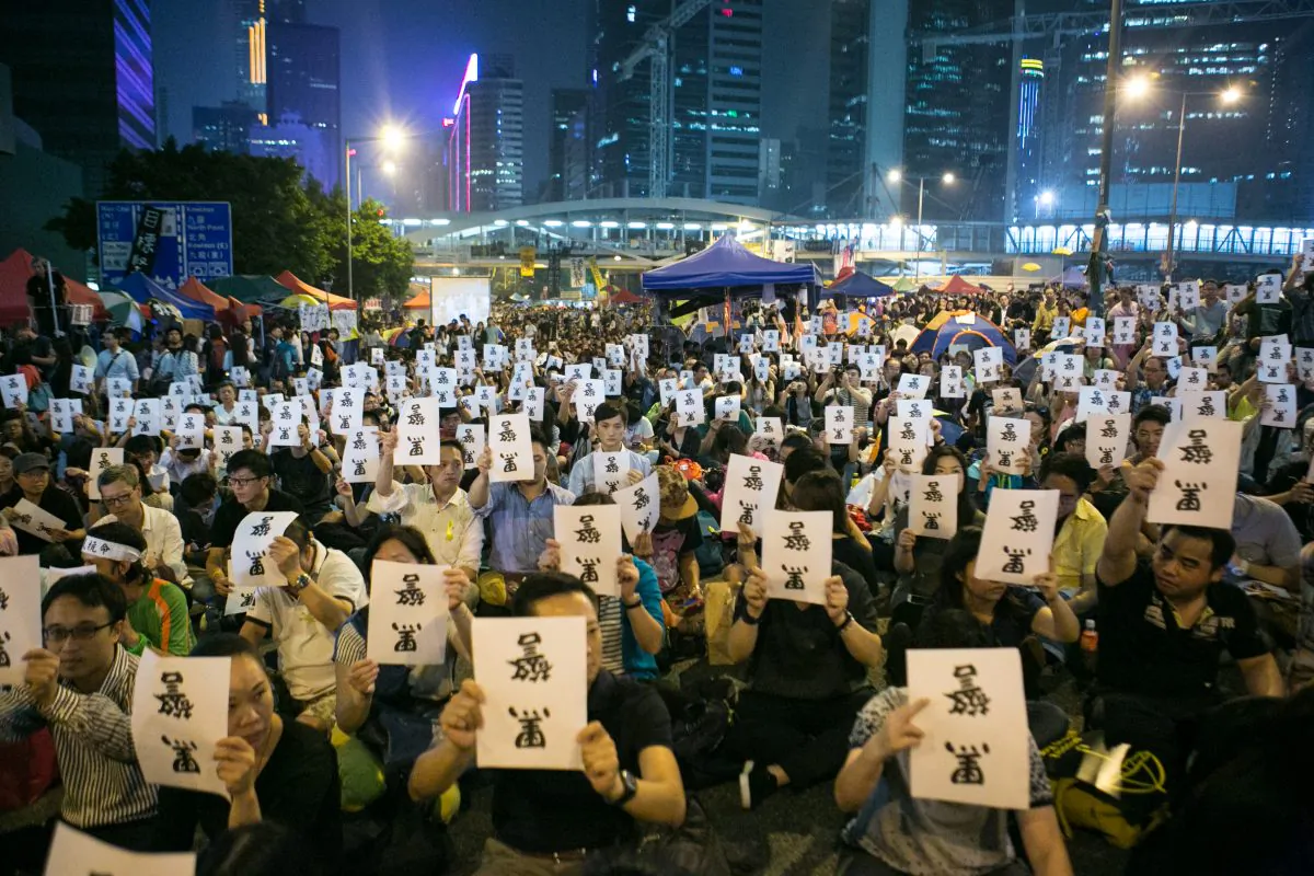 Thousands of pro-democracy protesters hold signs upside down that say in Chinese “Black Police,” referring to the incident in which police beat and kicked protesters as they removed them from Long Wo Road, on Oct. 15. (Benjamin Chasteen/Epoch Times)