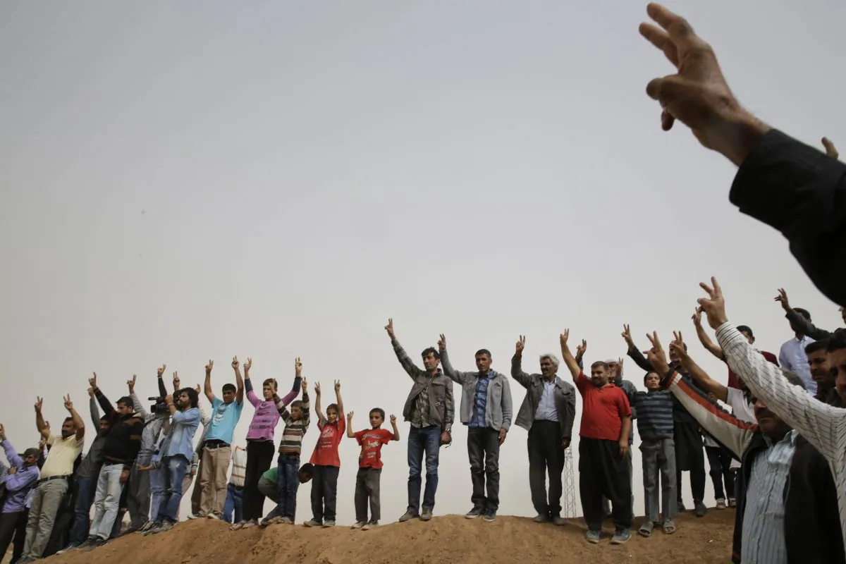 Kurdish mourners flash the V-sign as they sing a nationalistic Kurdish song at a cemetery in Suruc, on the Turkey-Syria border, during the funeral of two Syrian Kurdish fighters, names not available, who were killed in the fighting with the militants of the Islamic State group in Kobani, Syria, Saturday, Oct. 11, 2014. Kobani, also known as Ayn Arab, and its surrounding areas, has been under assault by extremists of the Islamic State group since mid-Sept. and is being defended by Kurdish  fighters. (AP Photo/Lefteris Pitarakis)