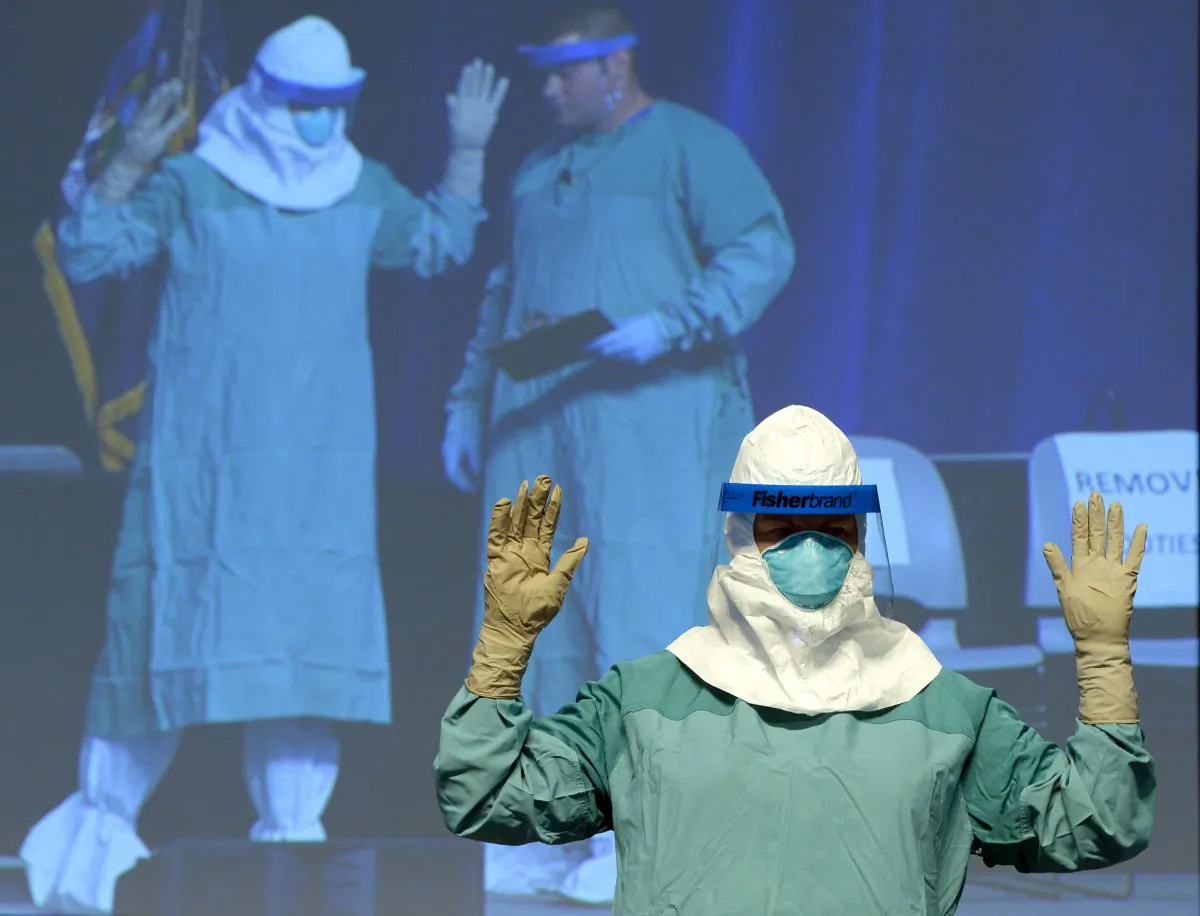 Barbara Smith, RN, Mount Sinai Health Sysytems and Bryan Christiansen MD,(monitor-R) CDC Infection Control Team for the Ebola Response demonstrate the proper technique for donning protective gear during an ebola educational session for healthcare workers at the Jacob Javits Center in New York on October 21, 2014.  (Timothy A. Clary/AFP PHOTO)  