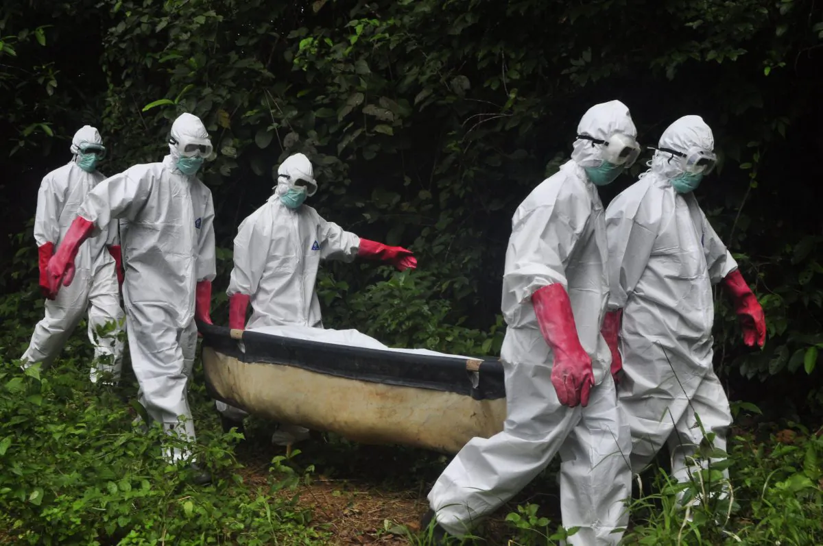 FILE - In this Saturday, Oct. 18, 2014 file photo, a burial team in protective gear carry the body of woman suspected to have died from the Ebola virus in Monrovia, Liberia. (AP Photo/Abbas Dulleh, File)
