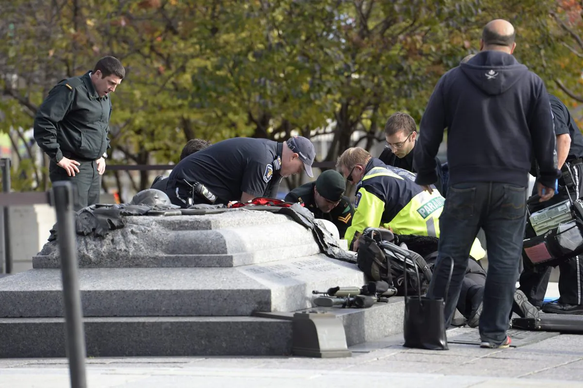 Emergency personnel tend to a soldier shot at the National Memorial near Parliament Hill in Ottawa on Wednesday Oct. 22, 2014.  The soldier was standing guard when an unknown gunman shot him. The gunman reportedly ran towards Parliament Hill, which is currently under lockdown and surrounded by security.  Prime Minister Stephen Harper was rushed away from the building to an undisclosed location, officials in his office said. (AP Photo/The Canadian Press, Adrian Wyld)