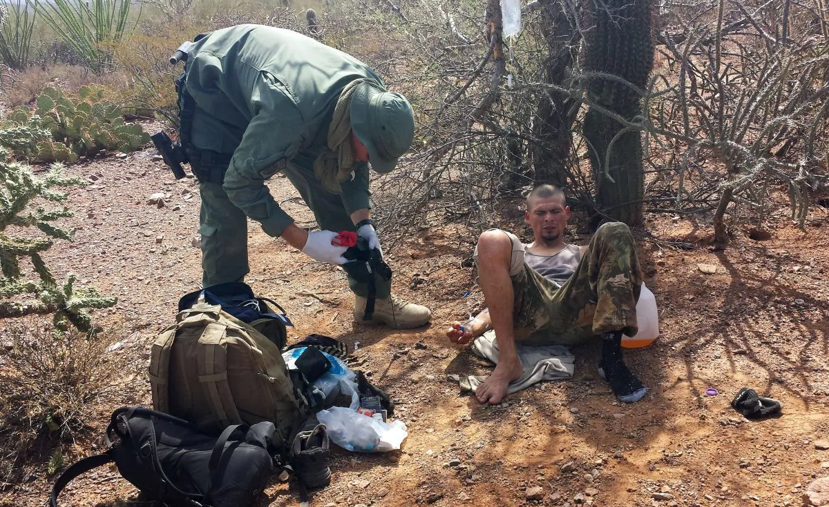 An unidentified US Border Patrol agent (L) helps an immigrant, including setting up intravenous fluid replacement for dehydration, near Sells, Ariz., on June 25, 2014. The number of migrants who died or needed rescue while crossing the desert from Mexico into Arizona has dropped significantly this year. (AP Photo/Astrid Galvan)