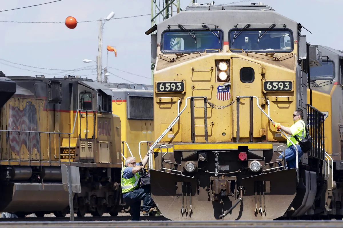 A train (L) operator dismounts a Union Pacific locomotive while another operator climbs up, at a rail yard in Council Bluffs, Iowa., on June 6, 2014. (AP Photo/Nati Harnik)