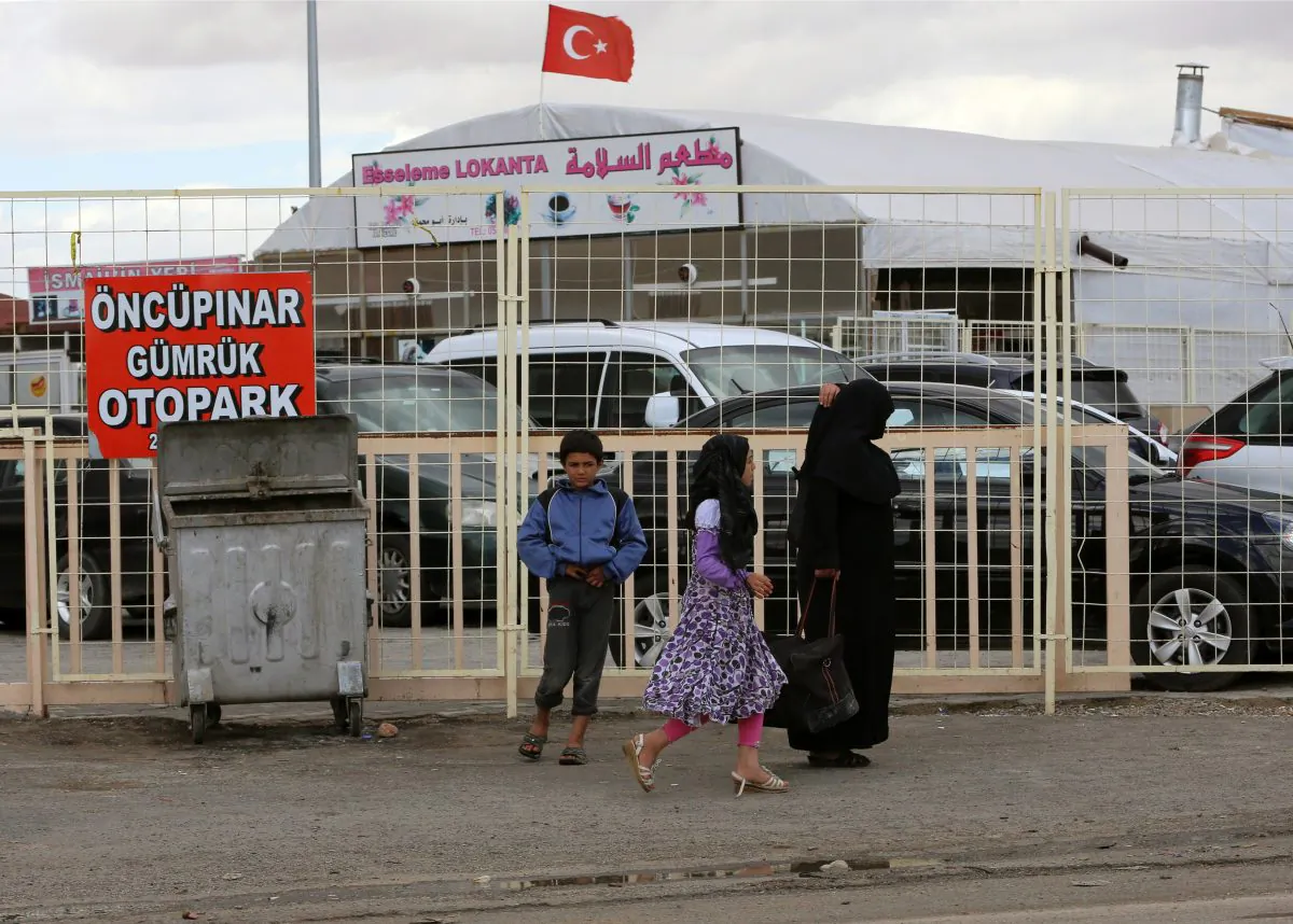 FILE - In this Sept. 28, 2014 file photo, Syrians are seen at the Turkish border crossing of Oncunipar, Kilis, Turkey. The Turkish border crossing of Oncunipar, an hour’s drive from the embattled Syrian town of Aleppo, is a chaotic buzz of people waiting to pass into one of the most violent regions in the world. Border guards stand by with machine guns to prevent Islamic militants from joining the flow, but within their sight smugglers offer to take travelers across for a surprisingly small fee. (AP Photo/Burhan Ozbilici, File)