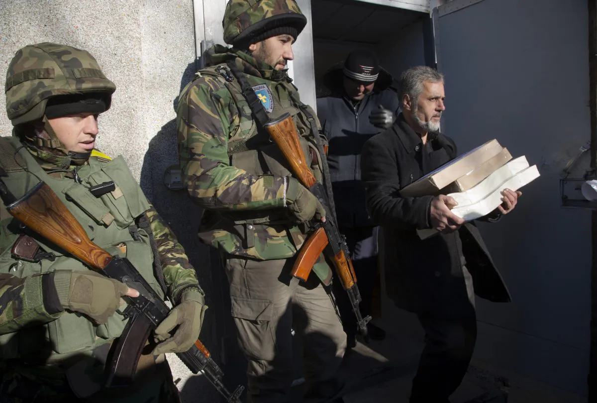 Ukrainian army soldiers guard a district election commission as an election official carries ballots to a polling station in Volnovakha, a village on the front line of fighting between Ukrainian government forces and rebels, eastern Ukraine, on Saturday, Oct. 25, 2014. (AP Photo/Dmitry Lovetsky)