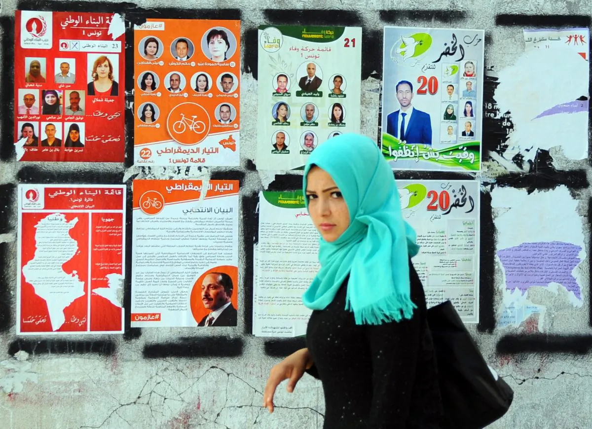 A woman walk past electoral campaign posters for the upcoming parliamentary elections in Tunis, Tunisia, Thursday, Oct. 23, 2014. Tunisians will flock to the polls on Sunday, Oct. 26, 2014, to elect representatives for a four year parliament in one of the final steps for the country's transition to democracy after overthrowing its leader more than three years ago. (AP Photo/Hassene Dridi)
