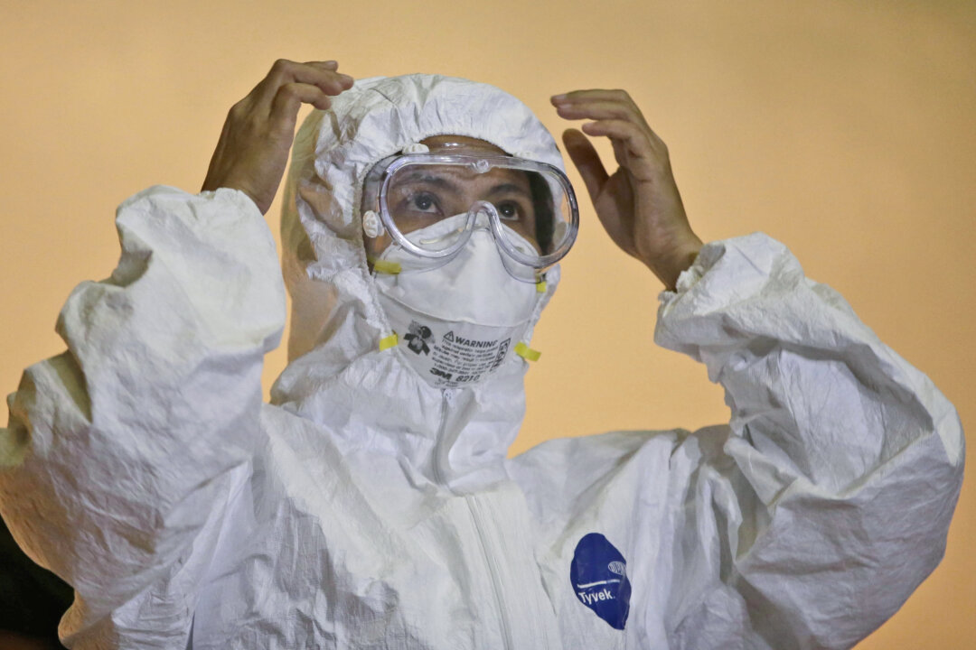 A health worker shows the proper way to wear an "Ebola suit" during a media tour of the Research Institute for Tropical Medicine facility to show the Philippine government's readiness in the still Ebola-free country at Alabang, Muntinlupa city, south of Manila, Philippines, on Oct. 21, 2014. The longer the Ebola outbreak rages in Africa, the greater chance a traveler infected with the virus touches down in an Asian city. (AP Photo/Bullit Marquez)