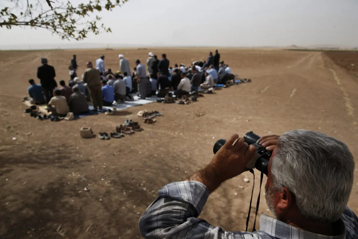 A Turkish Kurd, standing in Mursitpinar, Turkey, on the Turkey-Syria border, uses binoculars to watch intensified fighting over the border in Kobani, Syria, between Syrian Kurds and the militants of Islamic State group, as Turkish Kurds offer their Muslim Friday prayers, on Oct. 10, 2014. The predominantly Kurdish town of Kobani has been transformed from a dusty backwater into a symbol of resistance for Kurds around the world. The battle is now playing out in Kobanis streets and alleyways - a fight being watched by scores of Syrian and Turkish Kurds, as well as dozens of journalists, through binoculars from hilltops and farms just across the border in Turkey. The international media spotlight, has helped turn the defense of Kobani into a very public test for the American-led international effort to roll back and ultimately destroy the Islamic State group. (AP Photo/Lefteris Pitarakis)