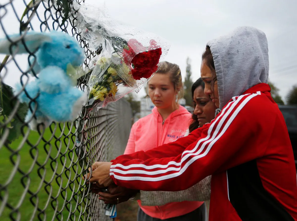 Marysville Pilchuck student Tyanna Davis (R) places flowers on the fence bordering Marysville Pilchuck High School in Marysville, Wash., Saturday, Oct. 25, 2014. A student opened fire in a high school cafeteria north of Seattle on Friday, killing at least one person and shooting several others in the head, officials said. The gunman also died in the attack. (AP Photo/The Herald, Mark Mulligan)