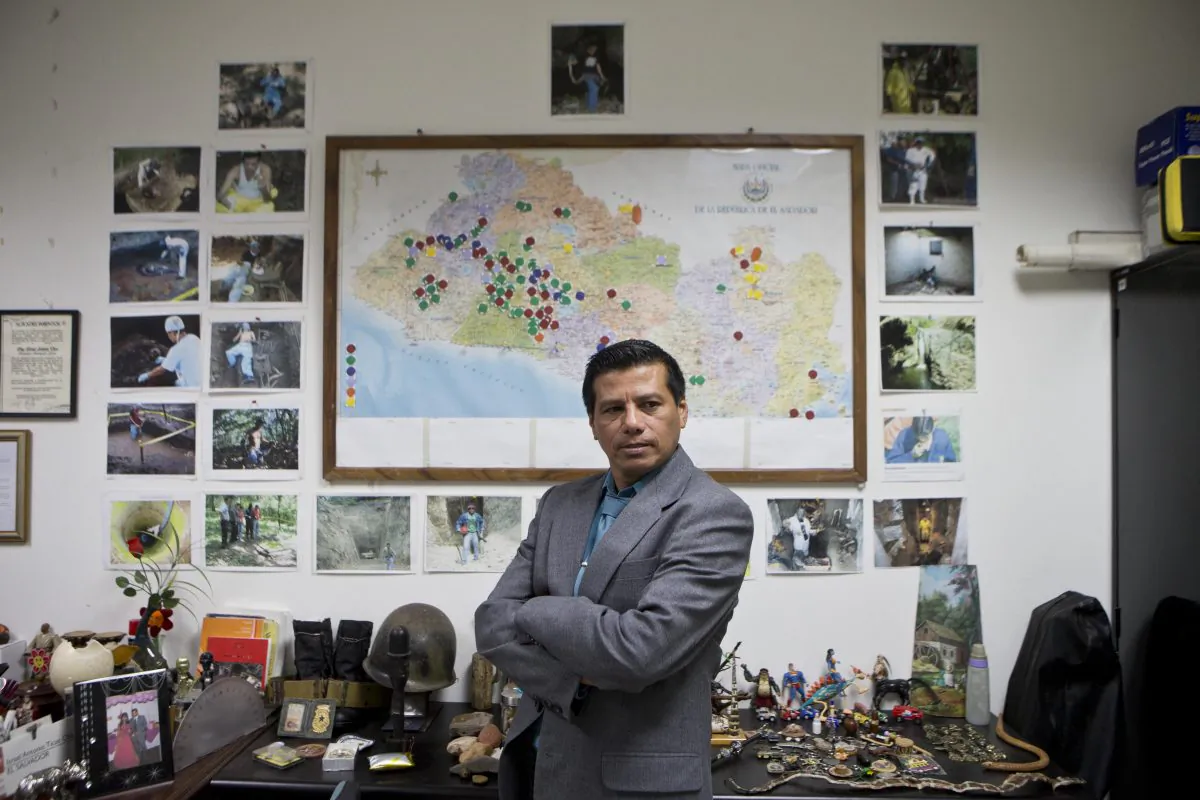 Criminologist Israel Ticas poses for backdropped by a wall papered with images of his team members at work and a map of El Salvador marking points of reported violent cases, in San Salvador, on Aug 20, 2014. Ticas calls himself the lawyer for the dead, who sees the evidence of gang rape and sadistic methods of murder on a daily basis. (AP Photo/Esteban Felix)