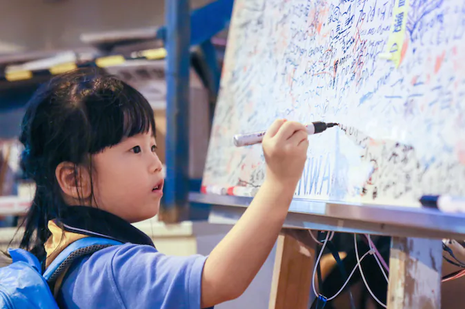 A little girl draws on a whiteboard that is filled with messages of hope and peace at what protesters are calling "Umbrella Square," in the Central District of Hong Kong, on Nov. 1, 2014. (Benjamin Chasteen/Epoch Times)
