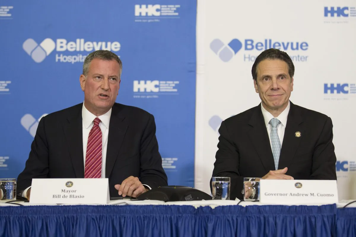 New York City Mayor Bill de Blasio (L) joins New York Gov. Andrew Cuomo at a news conference at Bellevue Hospital in New York, Oct. 23, 2014, after New York City physician Dr. Craig Spencer had tested positive for the Ebola virus. De Blasio has received high marks from pundits, who praise his reassuring, consistent tone when discussing the disease, a sharp contrast to the haphazard, and at times borderline hysterical, tone from Cuomo and New Jersey Governor Chris Christie. (AP Photo/John Minchillo)